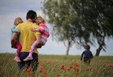 father holding two daughters and looking at his son running in front of them