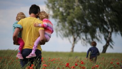 father holding two daughters and looking at his son running in front of them