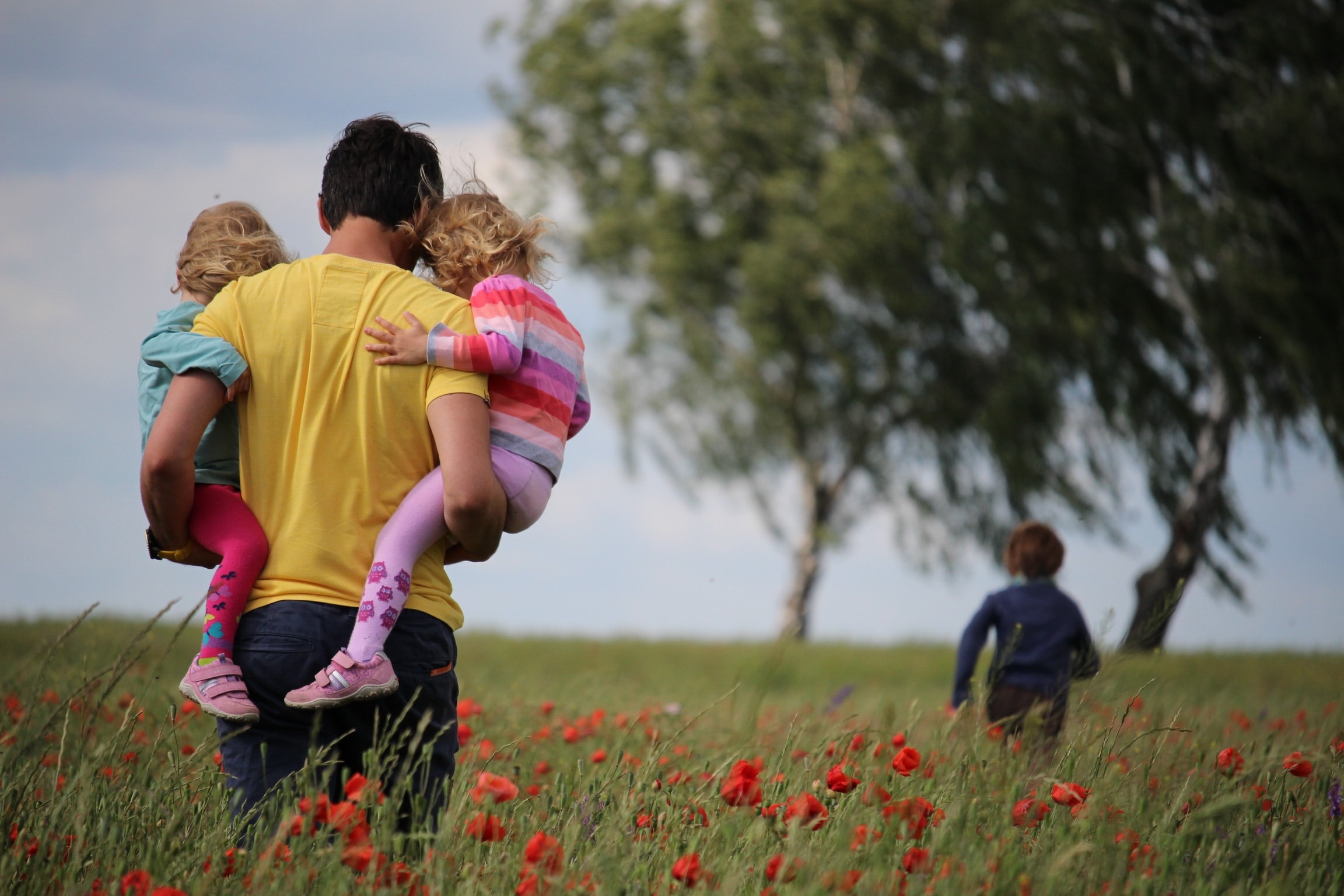 father holding two daughters and looking at his son running in front of them