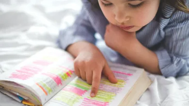 Little girl reading from Bible while lying in bed