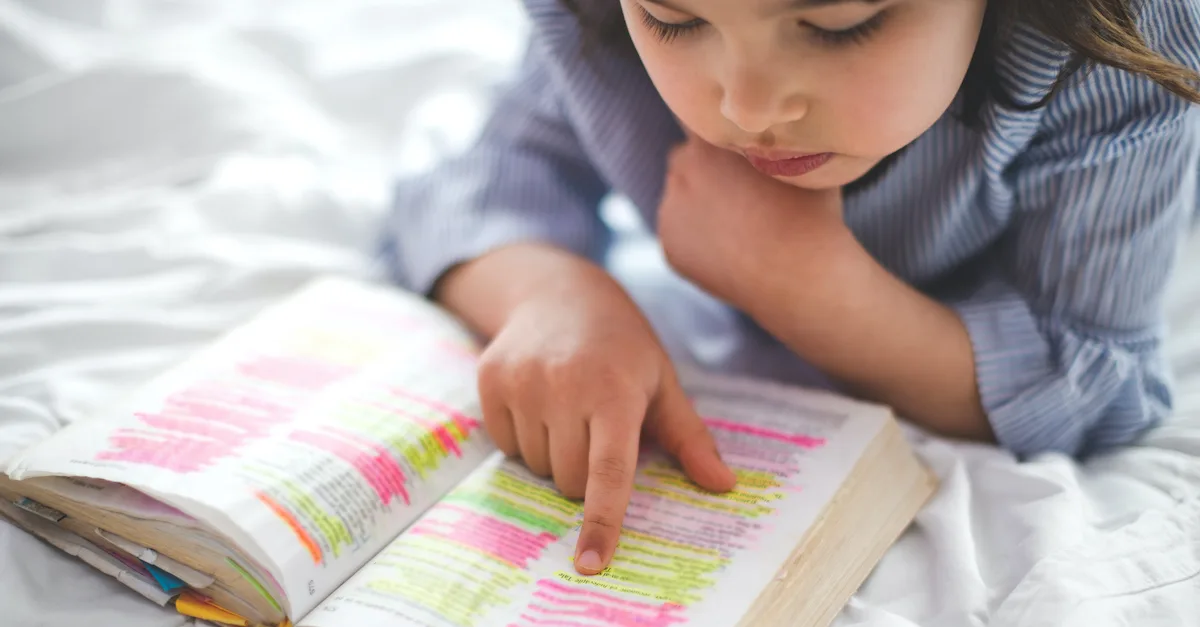 Little girl reading from Bible while lying in bed